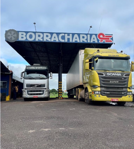 Dois caminhões estacionados lado a lado sob a cobertura da borracharia